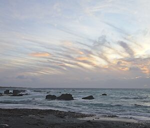 Sunset or sunrise over a bay, with heavy cloud on the horizon, becoming stripey and wispy high in the sky