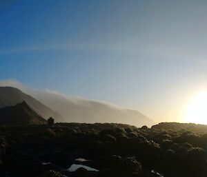 A wispy sweep of cloud over the plateau with bright sun to the right