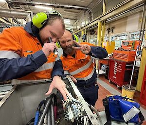 Two men in high vis inspect wiring in a box
