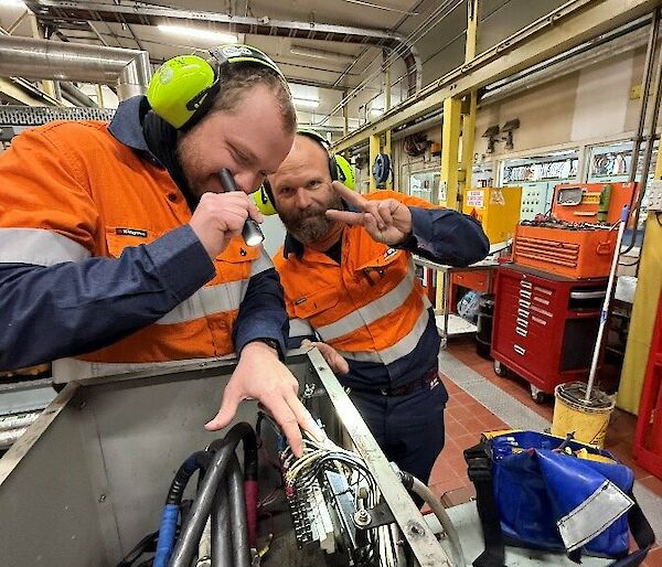 Two men in high vis inspect wiring in a box