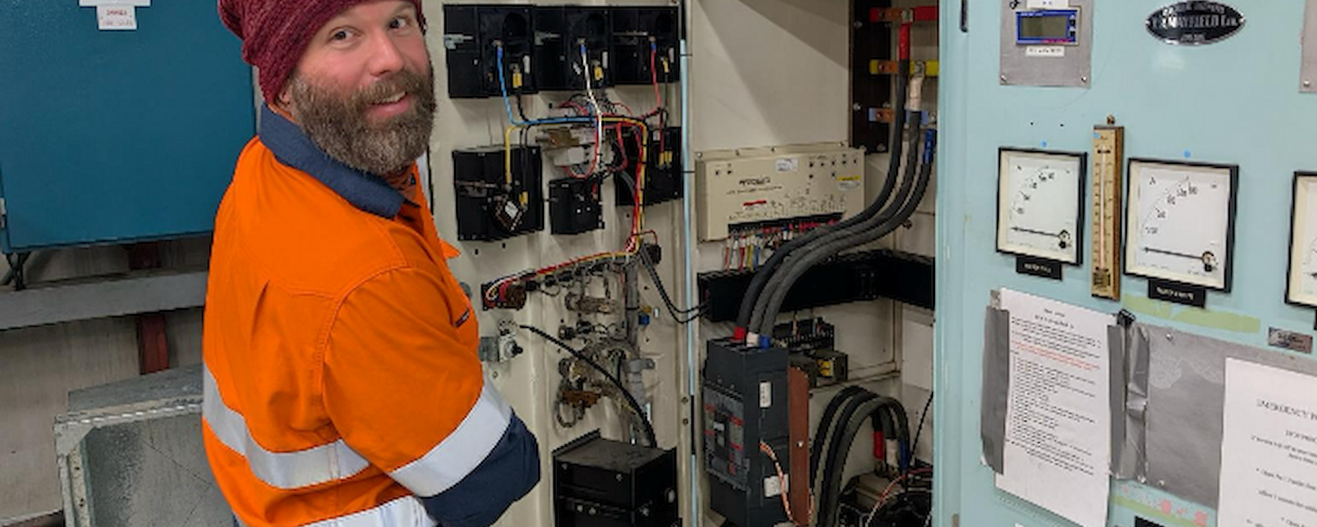 A man in high vis looks into a cupboard full of wiring