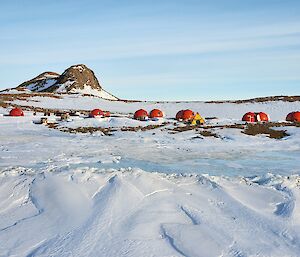 snowy landscape with rocky hills in the background and orange hard melon tents in the foreground