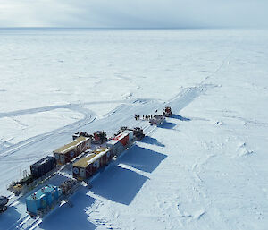 Aerial shot of a convoy of Antarctic tractors moving over a plain of snow and ice