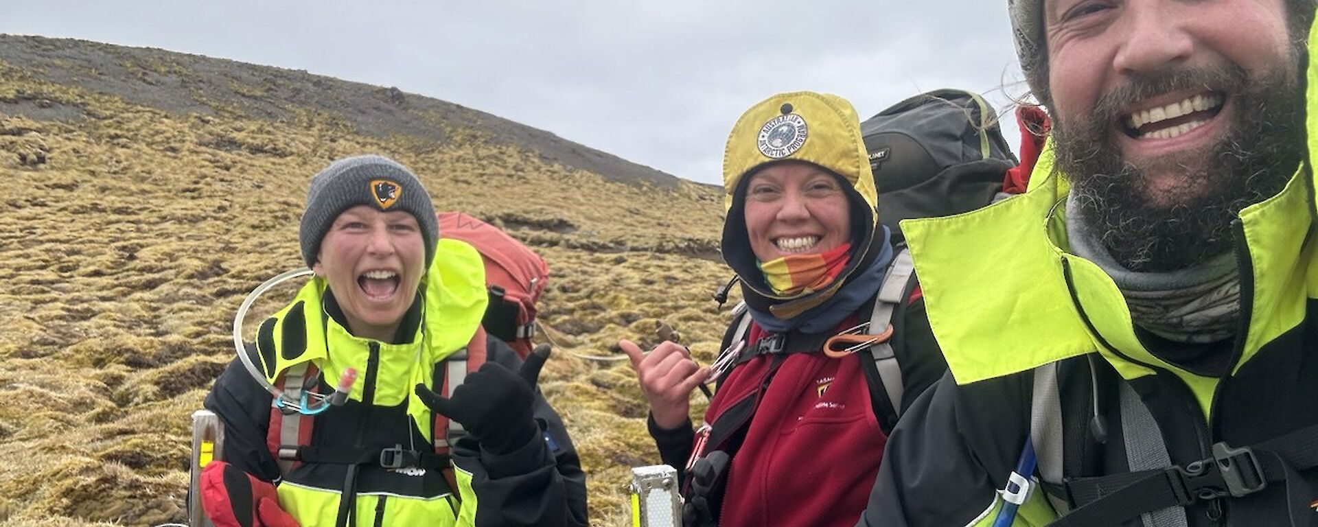 Three smiling people on a hillside with a track sign