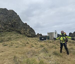 A person in hi vis on a hillside with a small white hut in the background