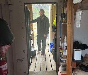 A smiling man stands in the doorway of a hut
