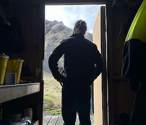 The back view of a man standing in a hut doorway looking out