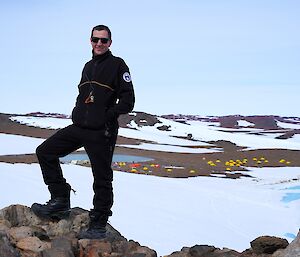 Expeditioner stands on rock in foreground with the Bunger Hills camp in the far background.