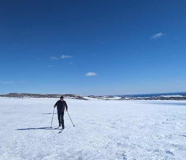 Expeditioner on skis. Blue sky background with snowy ground filling the majority of the photo. rocky mounds align with the horizon.