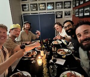 Image of 6 expeditioners sitting at dinner table with wine and food.