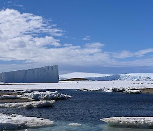 Beautiful vista showing steep ice cliffs to the left and cold blue green water in the foreground, under a blue sky
