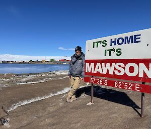 A person stands next to a sign saying 'It's Home It's Mawson'