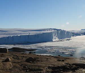 Steep ice cliffs to the left with a rocky slope in the foreground