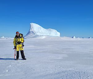 A man standing with an ice axe on ice, with an iceberg behind