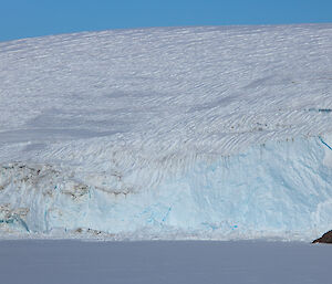 A wall of ice sloping down to a sea ice-covered ocean