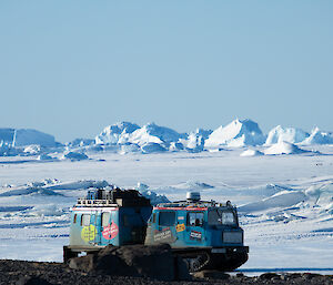 A blue Hägglunds vehicle parked on rocky ground with ice sloping up behind