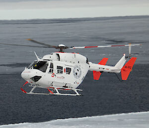 A white helicopter hovering over sea ice