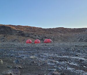 3 red melon huts on rocky ground
