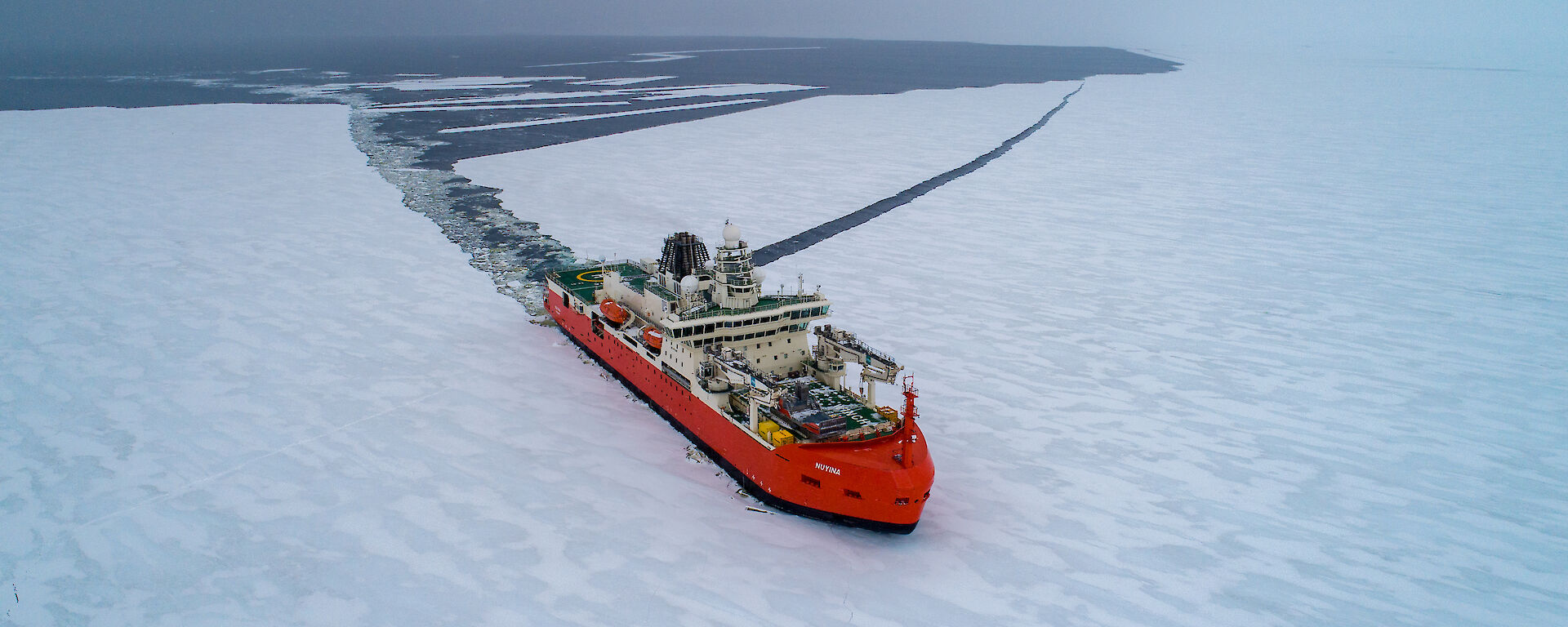 A red icebreaker ship cuts a swathe through the ice