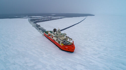 A red icebreaker ship cuts a swathe through the ice