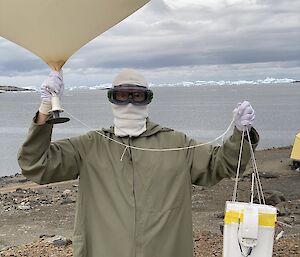A person, outside in protective clothing holding a large, white balloon.