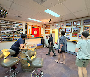 A group of fellows play darts in a recreation room
