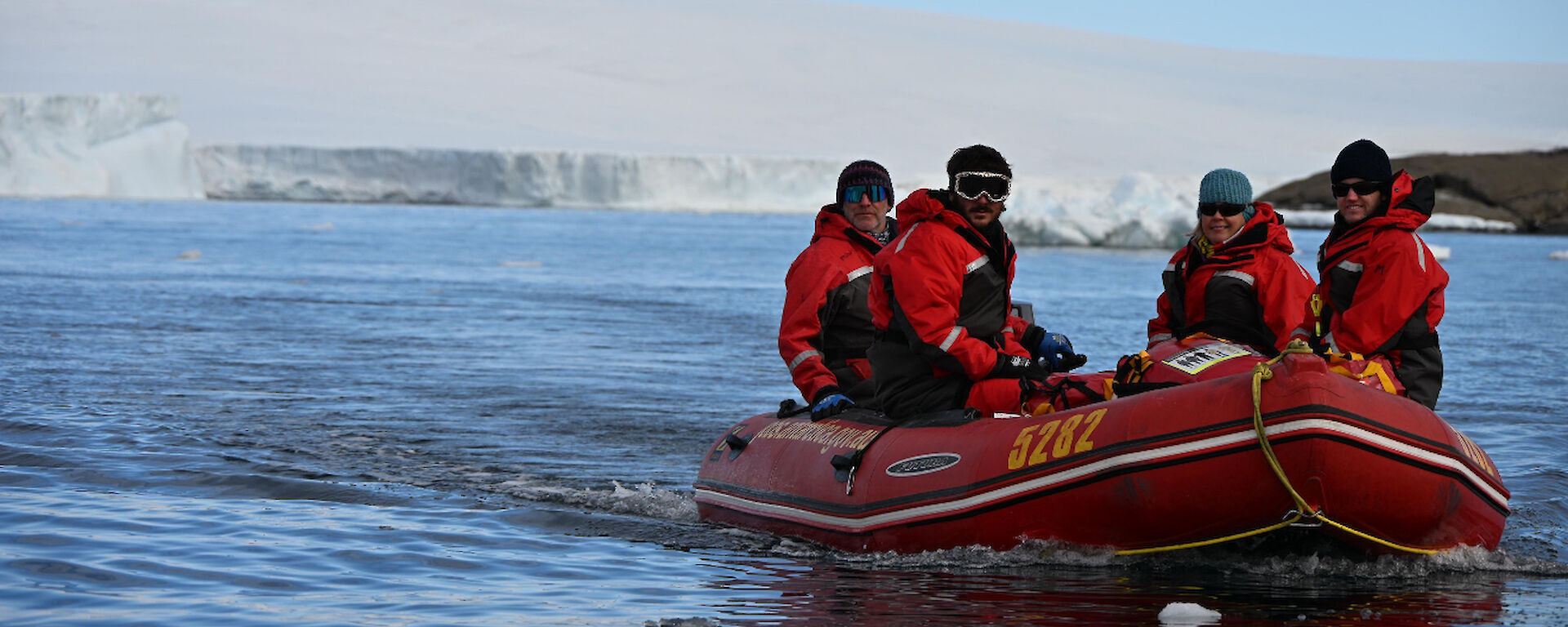 A group of people in a red rubber boat with snowy peaks behind them