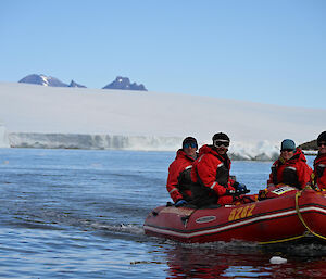 A group of people in a red rubber boat with snowy peaks behind them