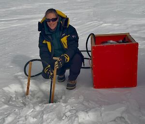 Image of a person kneeling on snow drilling into ice with a steam drill.