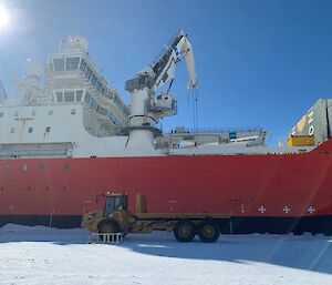 Big red and white ship parked up in the ice with the flat tray truck next to it