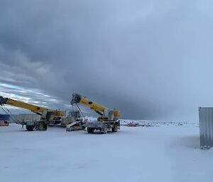 Two big yellow cranes with really ominous clouds above