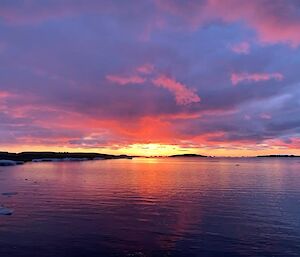 The same open bay but a dark orange sunset under dark purple clouds