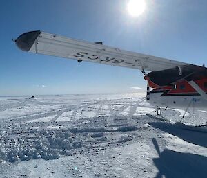 Left view of a small red and white ski plane, sitting on an endless plain with tyre tracks through it