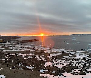 Sun going down with snow and rocks and a bay in the foreground