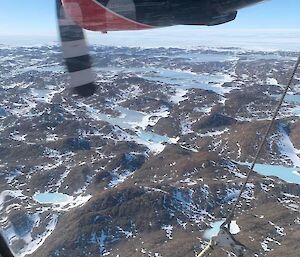 View from a plane of endless brown hills with lakes and snow scattered