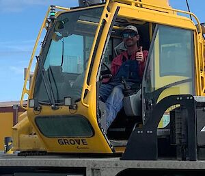 A man sits in a crane cabin smiling and putting his thumb up
