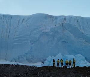 A group of expeditioners stand in front of a glacier