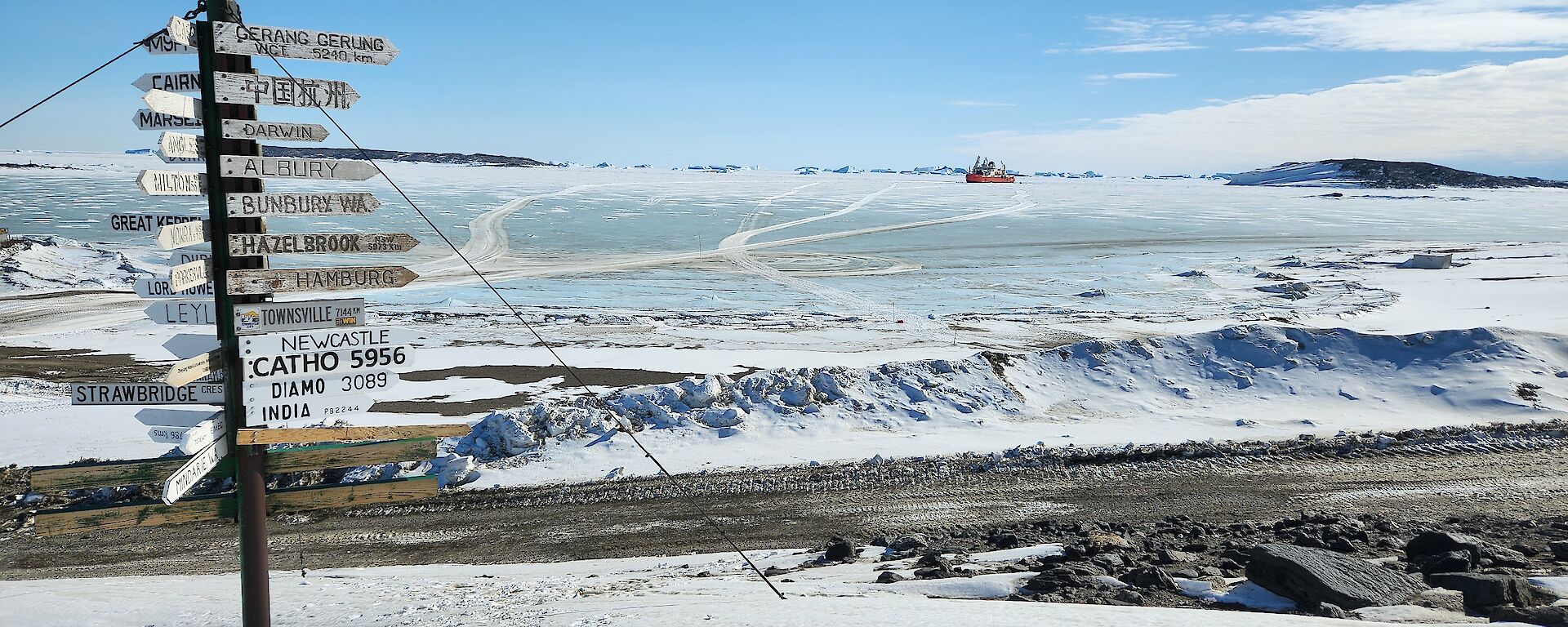 A signpost on the left, icy landscape and a red ship in the far distance