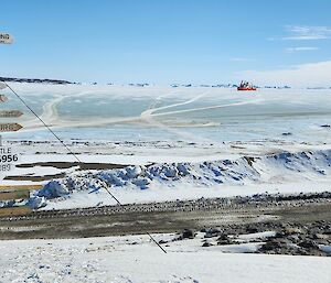 A signpost on the left, icy landscape and a red ship in the far distance