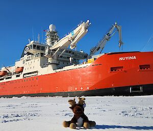 A big red icebreaker ship parked up in the ice with a stuffed reindeer toy in front of it