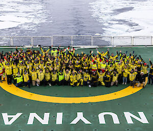 A group of people wearing yellow stand on the helicopter deck of a ship with the words NUYINA across it