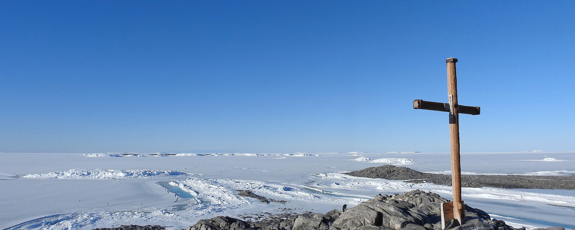 A wooden cross stands on a rocky hill looking out to endless snow and ice