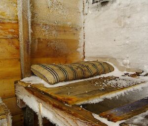An old plank bed with a pillow inside a wooden hut