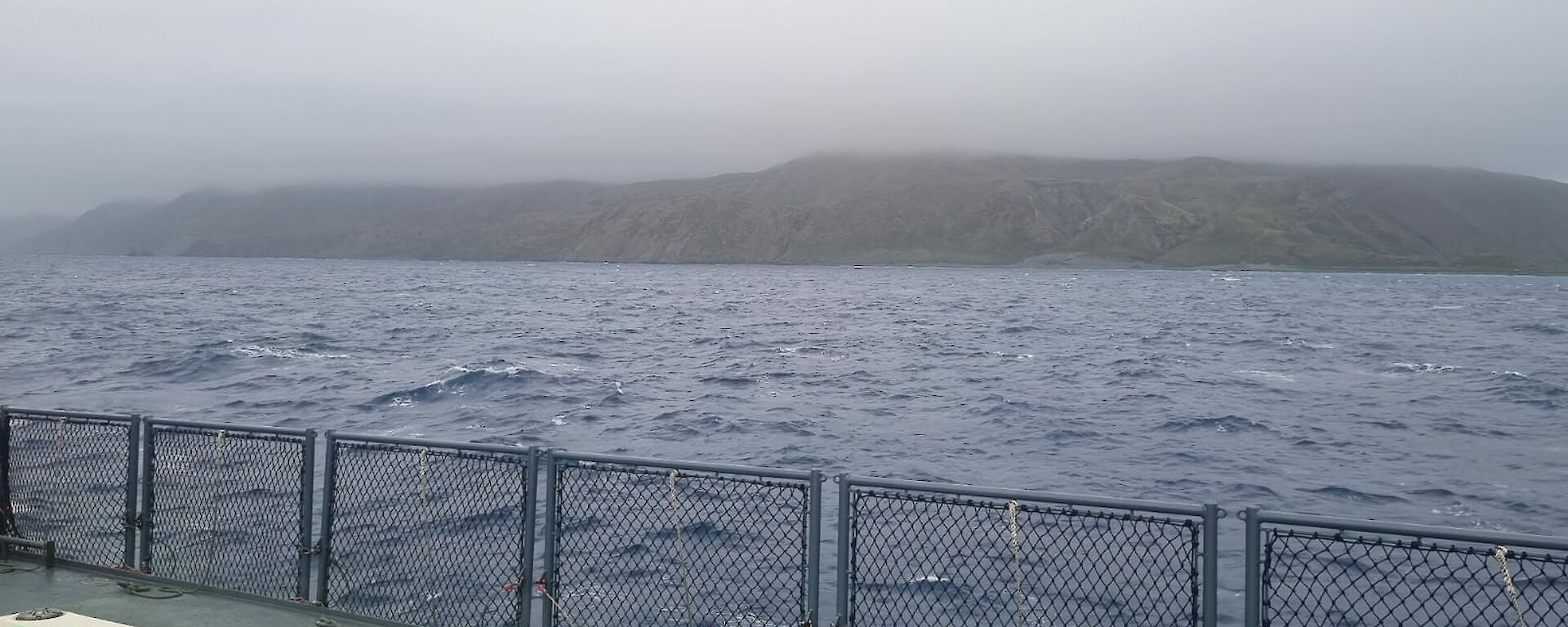 Looking across sea from deck of ship to island shrouded by cloud