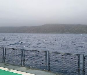 Looking across sea from deck of ship to island shrouded by cloud