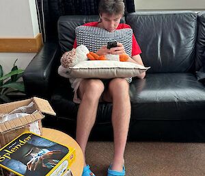 Image of expeditioner sitting on black gouch cuddling stuffed toy.