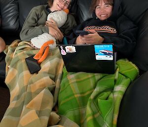 Image of two girls sitting on couch hugging plush toy, watching movies on laptop.