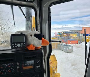 Image of plush toy inside dozer on dashboard. Background features shipping containers stacked surrounded by snow.
