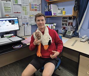 Image of plush toy draped around expeditioner's neck - sitting in front of computer and desk.