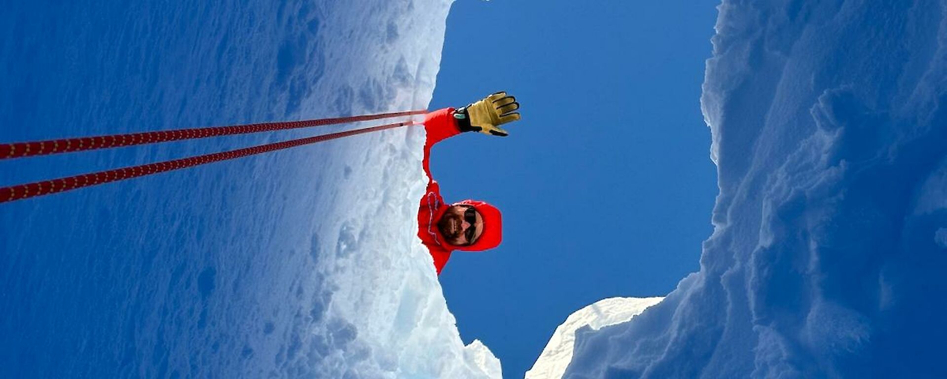 Image of a field training officer (FTO) standing above a crevasse in the ice looking down at a glaciologist.